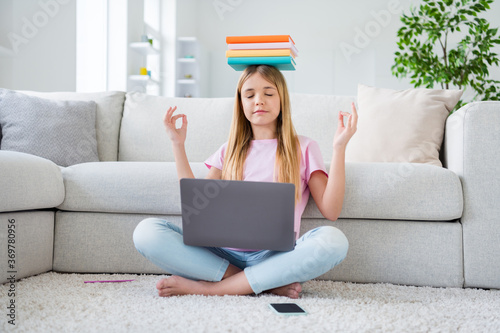 Full size photo of focused little kid study remote laptop hold pile books lesson materials head meditate before online communication sit floor legs crossed folded in house indoors