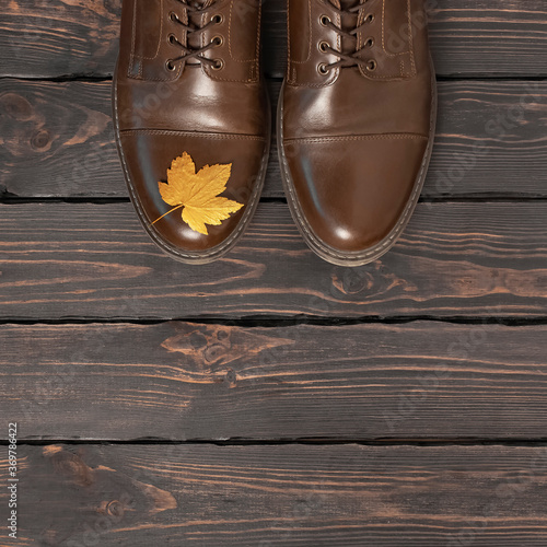 Brown classic leather men's shoes and autumn golden leaves on dark wooden background top view. Autumn Fashion Concept. Fashionable male footwear. Cozy fall composition. Sale, shoe advertising