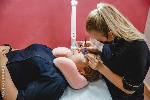 Eyelash Extension process. Master in black uniform does procedure in the beauty salon.