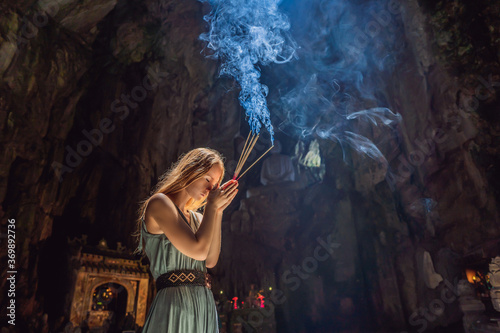 Young woman praying in a Buddhist temple holding incense Huyen Khong Cave with shrines, Marble mountains, Vietnam
