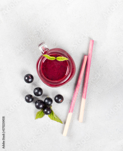 Berry drink, blackcurrant smoothie in a jar with a bamboo straw on a light background top view