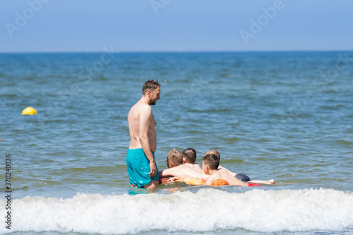 Mężczyzna pilnuje dzieci pływających na dmuchanym materacu w morzu