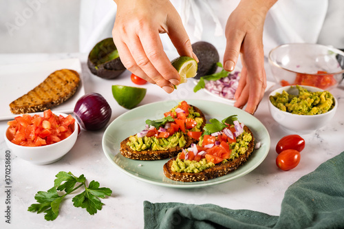 Close up of woman's hands squeezing a slice of lime on mashed avocado toast in a green plate