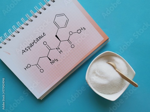 Structural chemical formula of aspartame molecule with artificial sweetener in white bowl. Aspartame is an artificial sweetener used as a sugar substitute in low-calorie food and drinks.