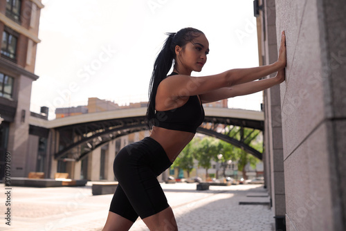 Young woman warms up and stretches her arms against a wall outside the morning sport. Health and Sport Concept.