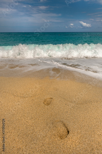 wakacyjna pocztówka, gorący piasek, ślady stóp, ciepłe morze i niebieskie niebo