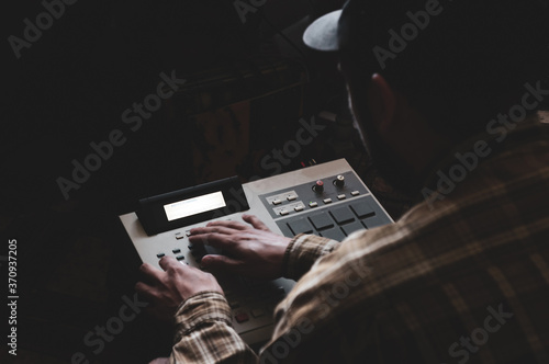 A hip hop composer, beatmaker creates beats on a digital production controller with pushbutton pads. The DJ plays the beats live on the pad controller of digital audio equipment. Rap music 