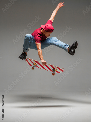 Cool young guy skateboarder jumps on skateboard in studio on grey background. Photography about skateboarding tricks