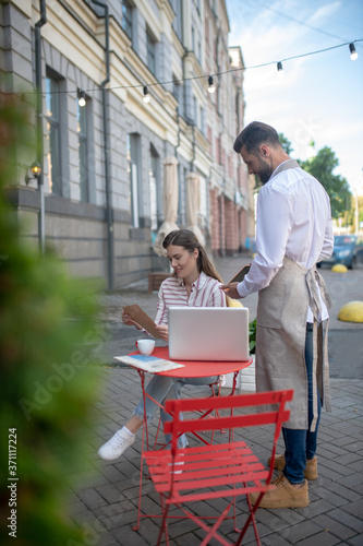 Brown-haired female studying menu, bearded waiter waiting for her order