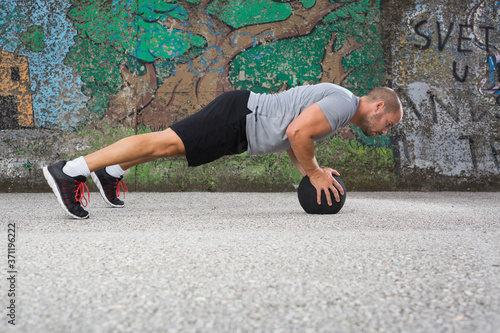 Sportist doing push-ups with a medicine ball outdoors.
