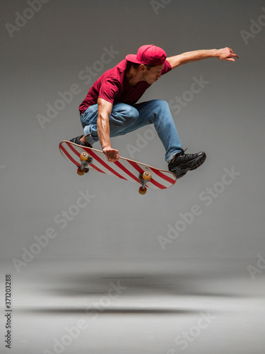 Cool young guy skateboarder jumps on skateboard in studio on grey background. Photography about skateboarding tricks
