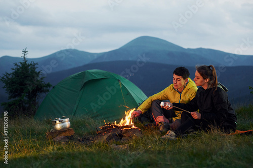 Classical marshmallow making near campfire. Young couple. Majestic Carpathian Mountains. Beautiful landscape of untouched nature