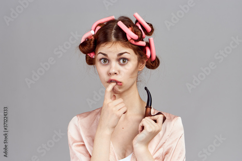 woman with curlers on her head in a dressing gown housewife smoking pipe in hand gray background