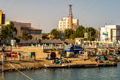 Port Sudan, Sudan. Busy coast in a harbor in Port Sudan, with sudanese people trading goods, exchanging, fishing, spending time and working. Old buildings of the city in the background.