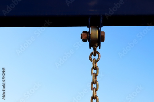 Metal construction with bolt and iron shiny thick chain against the blue sky . Metal chain of a swing set seat in soft high key focus