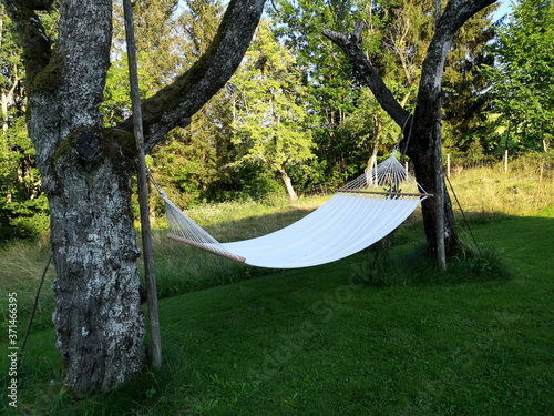 Schöne weiße Hängematte im Schatten zwischen zwei Bäumen im Sommer auf einem Bauernhof in Rudersau bei Rottenbuch im Pfaffenwinkel im Landkreis Weilheim-Schongau in Oberbayern