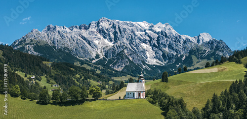 Panorama of green meadows and parish church of Dienten with Hochkönig mountain on the background. Pinzgau, Salzburg, Austria.