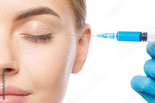 Headshot of young attractive woman pictured with eyes closed during botox injection procedure in beauty clinic, isolated on white background