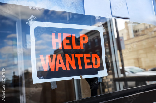 Reflection of a man looking at a help wanted sign in a business window, economy concept