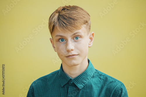portrait of a young man in a blue shirt with blue eyes on a yellow background