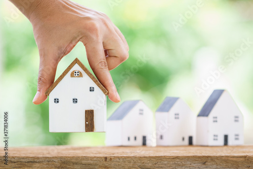 A woman shopping for a new home is hand hold at one of the houses on the table in the backyard, Saving money or loan for business Investment real estate concept.