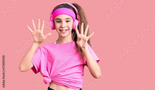 Cute hispanic child girl wearing gym clothes and using headphones showing and pointing up with fingers number nine while smiling confident and happy.