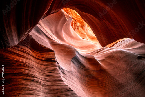 Moving towards the light of Lower Antelope Canyon in Page Arizona with natural landscapes of vibrant sandstones folded into flaky waves of fire in a narrow sandy labyrinth with caves