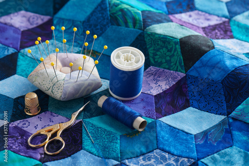 Pincushion, spools of thread, scissors and thimble on the tumbling blocks quilt background
