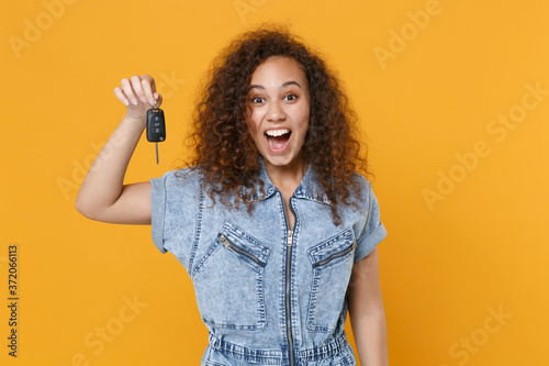 Surprised young african american girl in casual denim clothes posing isolated on yellow wall background studio portrait. People sincere emotions lifestyle concept. Mock up copy space. Hold car keys.