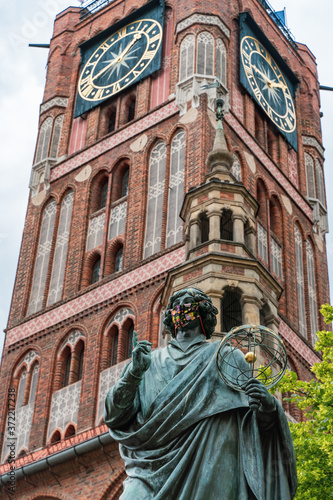 The Nicolaus Copernicus monument by Christian Friedrich Tieck unveiled in 1853 in Torun, Poland. The statue with the mask on beacause the virus pandemic. Brick tower of Thorn town hall in background.