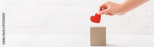 cropped view of female hand putting red heart in box on white background, donation concept