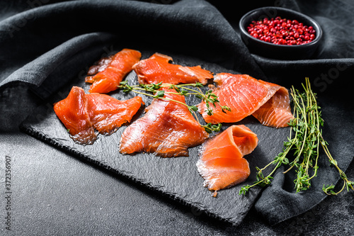 Salted salmon slices with pepper and thyme. Organic fish. Black background. Top view