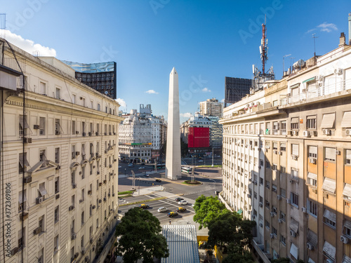 El Obelisco de Buenos Aires enmarcado por dos edificios coloniales y el skyline de la Av. 9 de julio con un cielo azul como fondo.