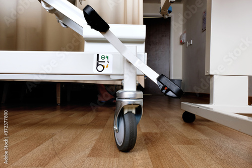 Brake pedal at the foot of a patient hospital bed with illustrated operation instruction where the lock mechanism can be engaged by pressing on the lever so that the bed does not roll or move.