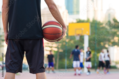 Closeup of basketball player holding a ball while watching the game on the sideline at an outdoor court in the city.