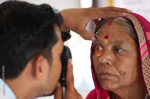 Old Indian woman in pink mantilla from Rajasthan getting eyes tested. Eye camp. Eye patient. Weak eyesight. Eye Health. Eye examination by doctor. Healthcare to elderly.