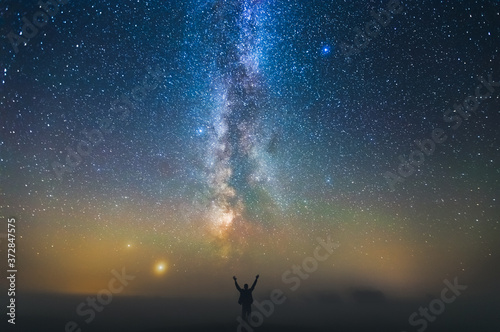 Landscape with Milky way galaxy and man standing against the stars, freedom concept