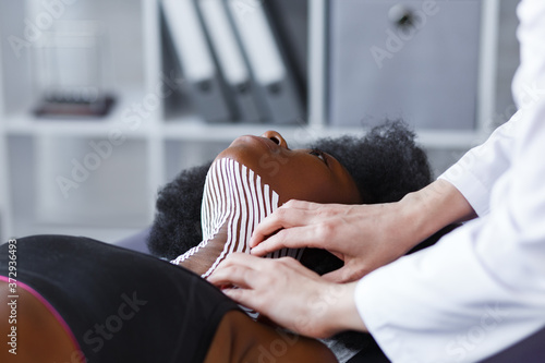 Kinesiology taping. Physiotherapist applying kinesiology tape to patient neck. Therapist treating young female African American athlete. Post traumatic rehabilitation, sport physical therapy.