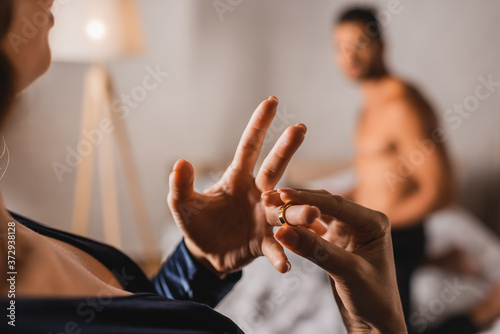 Selective focus of woman taking off wedding ring while standing near shirtless man in bedroom