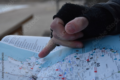 Mano con mitón señalando punto determinado en mapa turístico planificando ruta