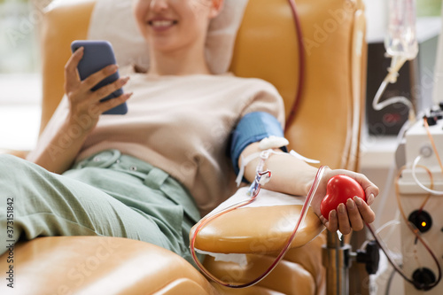 Close-up of young woman lying on the couch with mobile phone while donating blood at the laboratory