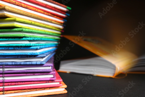 Domowa biblioteka - książki w kolorowych okładkach ułożone w kolumnie, otwarta książka w tle