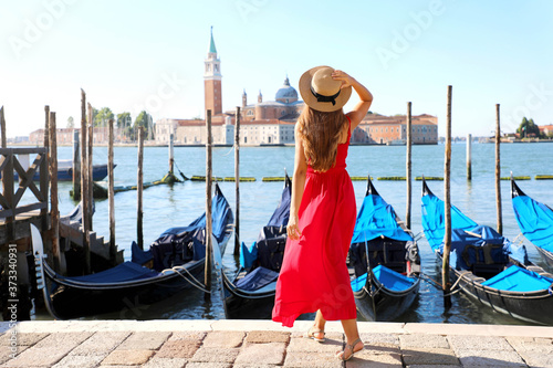 Back view of beautiful girl in red dress walking in Venice with gondolas moored