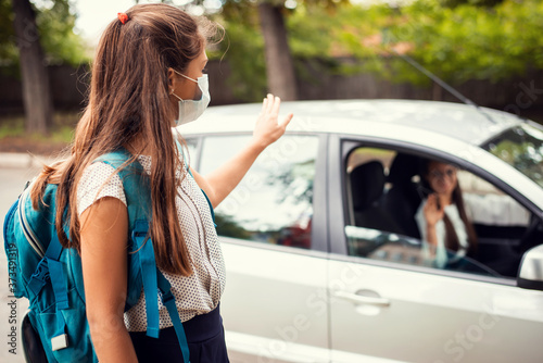 Mother in car, dropping off her daughter to the school and wishing her a good day. Back to school, motherhood concept.