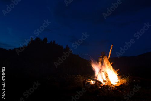 Summer camp fire and fir trees after sunset with the moon rising. Wanderlust concept. 