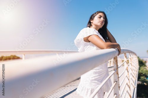 Young beautiful woman wearing hat leaning on a bridge and sunbathing