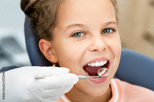 Little smiling girl, teeth check-up. Tooth exam using dental mirror close-up. Child's teeth treatment