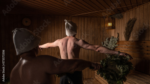A bather massages a man with a broom of oak and birch in a wooden sauna 
