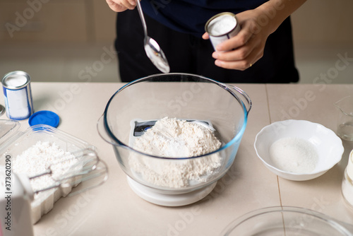 Woman adding bicarbonate soda to flour on a small kitchen scale while making cookies in the kitchen