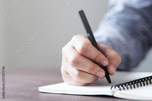 close up hand young man are sitting using pen writing Record Lecture note pad into the book on the table wood.